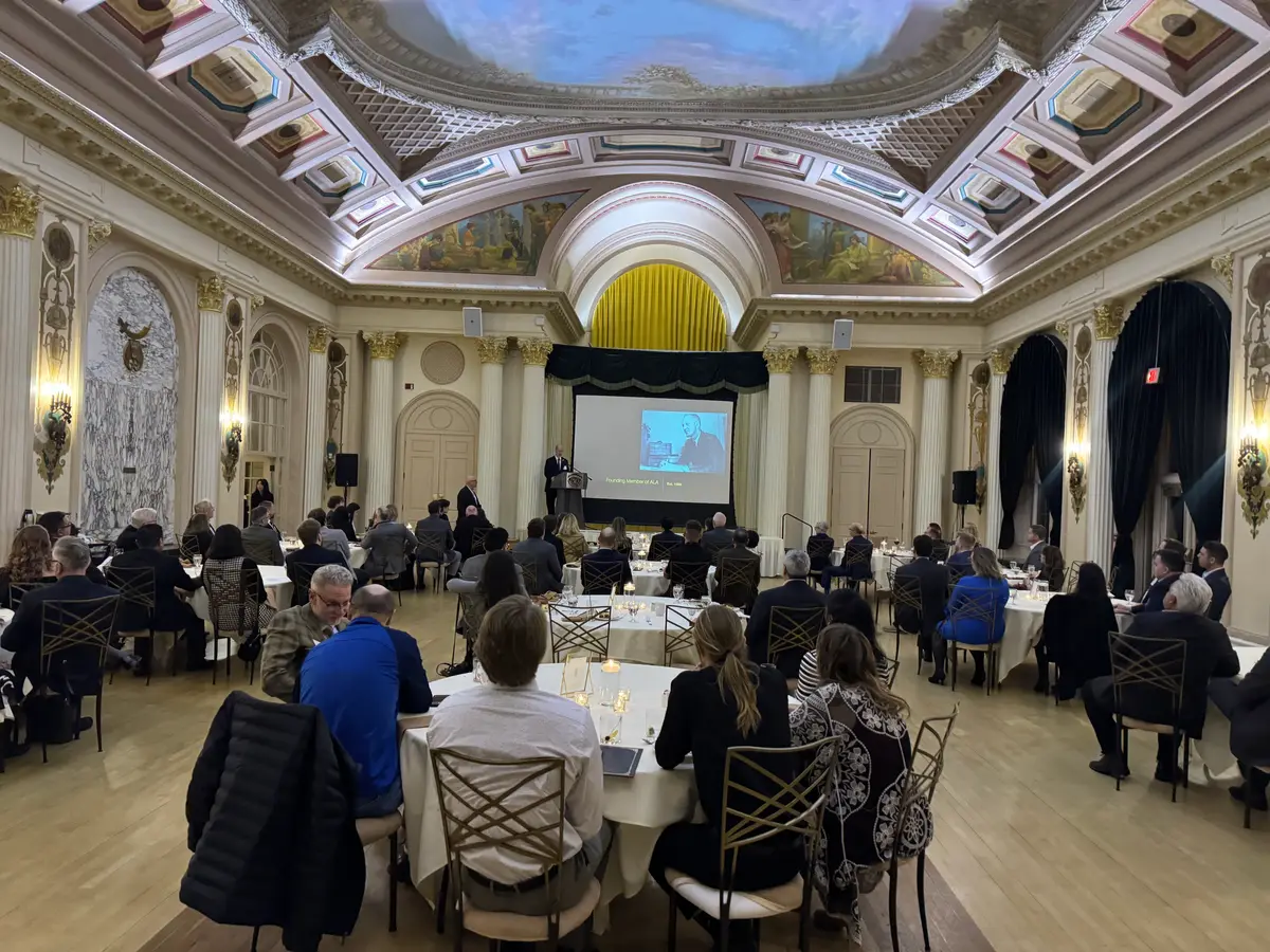 Association members seated at round tables in a historic ballroom while a speaker presents from the stage.